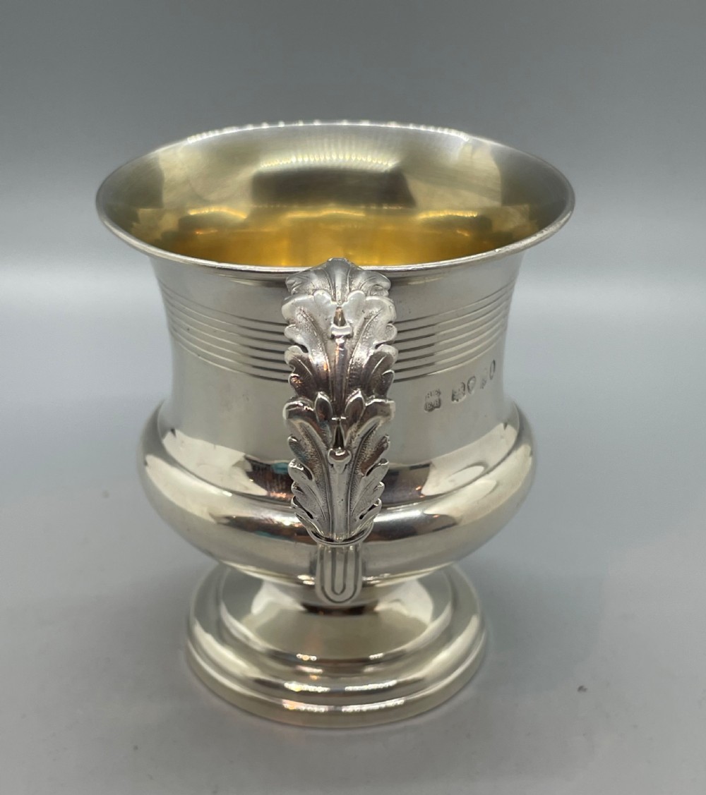 A George IV sterling silver mug featuring horizontal reeded decoration, a leaf-scrolled handle, a molded pedestal foot, and a gold-gilded interior. View III