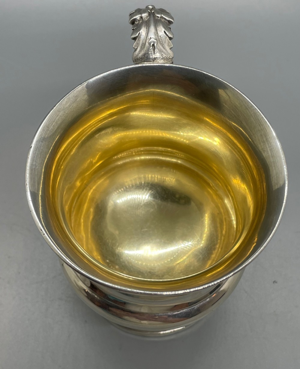 A George IV sterling silver mug featuring horizontal reeded decoration, a leaf-scrolled handle, a molded pedestal foot, and a gold-gilded interior. View VI