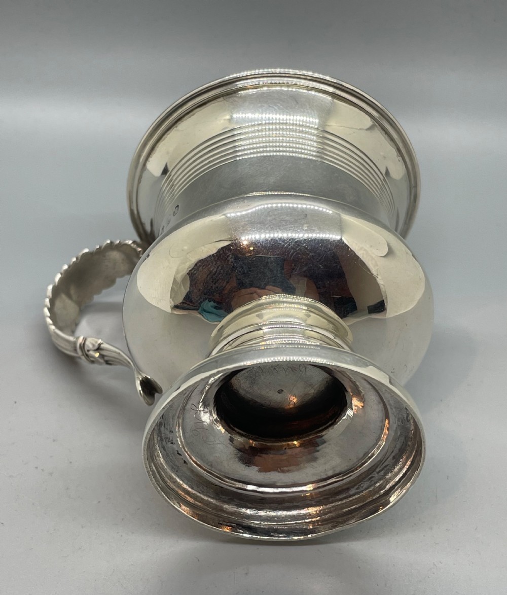 A George IV sterling silver mug featuring horizontal reeded decoration, a leaf-scrolled handle, a molded pedestal foot, and a gold-gilded interior. View VII