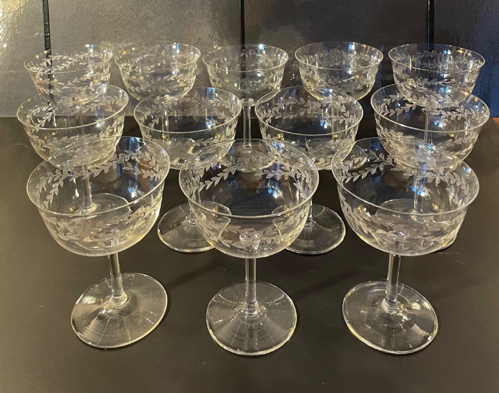 A set of twelve clear Edwardian glass champagne coupes featuring acid-etched laurel leaf garlands around the bowls. View V