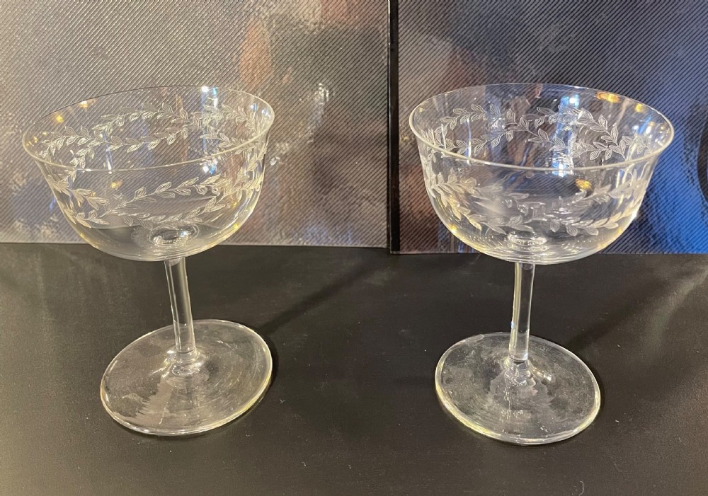 A set of twelve clear Edwardian glass champagne coupes featuring acid-etched laurel leaf garlands around the bowls. View VI