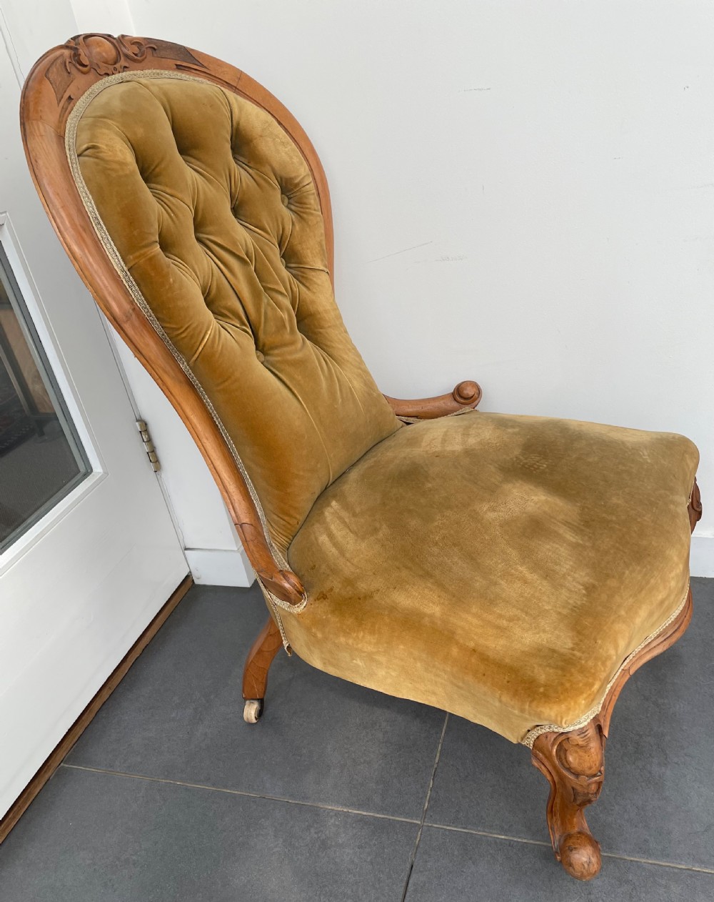 A Victorian walnut occasional chair featuring a spoon-shaped button-backed backrest upholstered in mustard velvet, supported by carved cabriole legs with ceramic castors. View VI