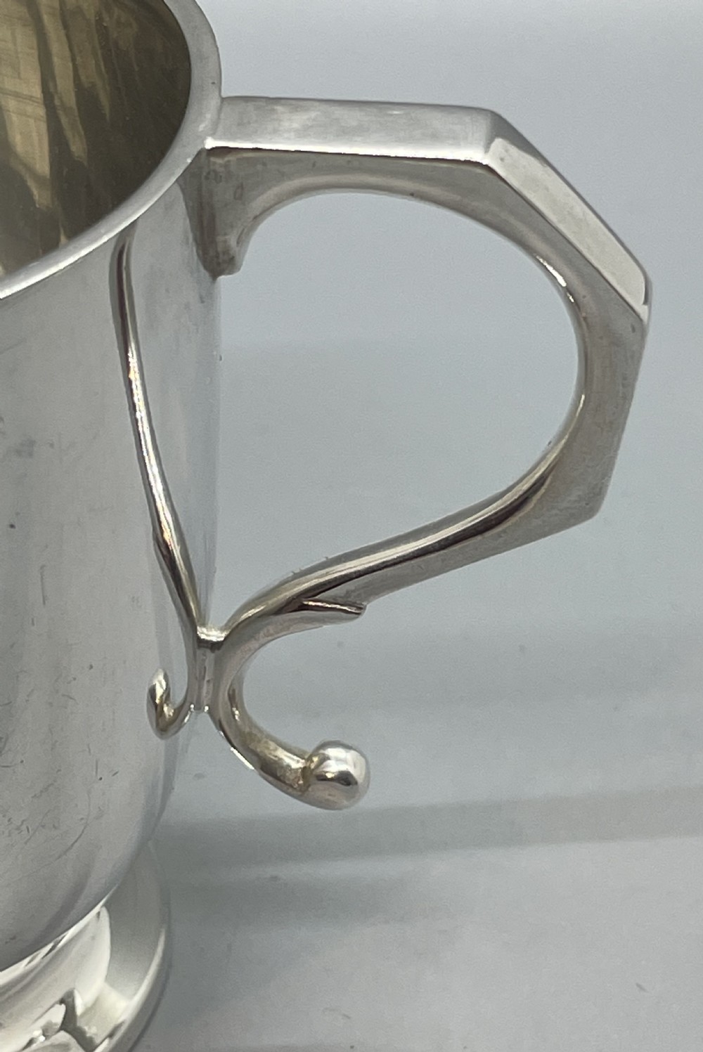 A solid sterling silver christening mug featuring a plain body, a stepped circular base, and an angular scroll handle. View VII