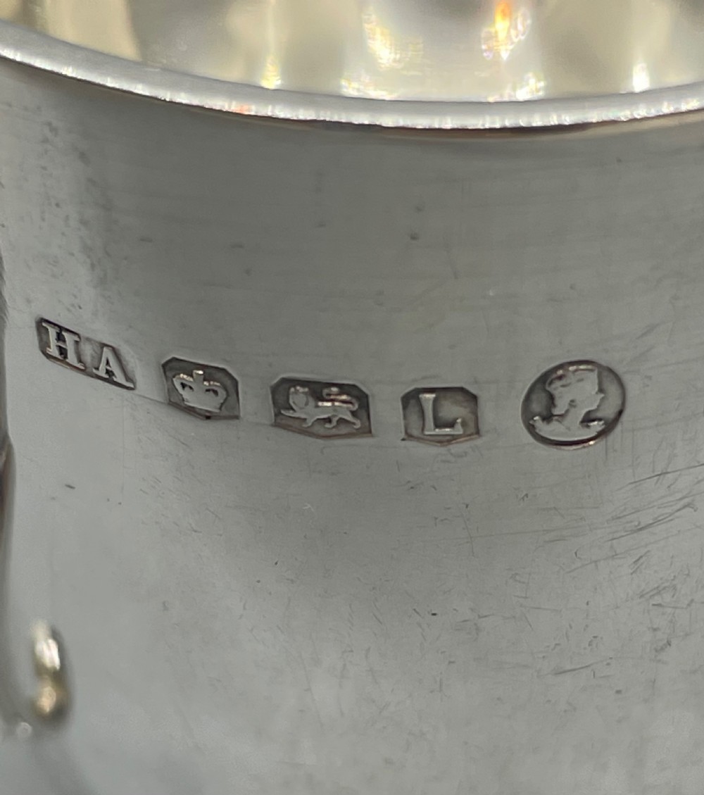 A solid sterling silver christening mug featuring a plain body, a stepped circular base, and an angular scroll handle. View VIII