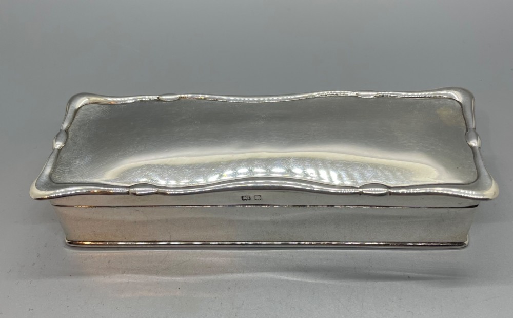 A rectangular Edwardian sterling silver box with a shaped, contoured lid rim and visible British hallmarks stamped on the front side. View II