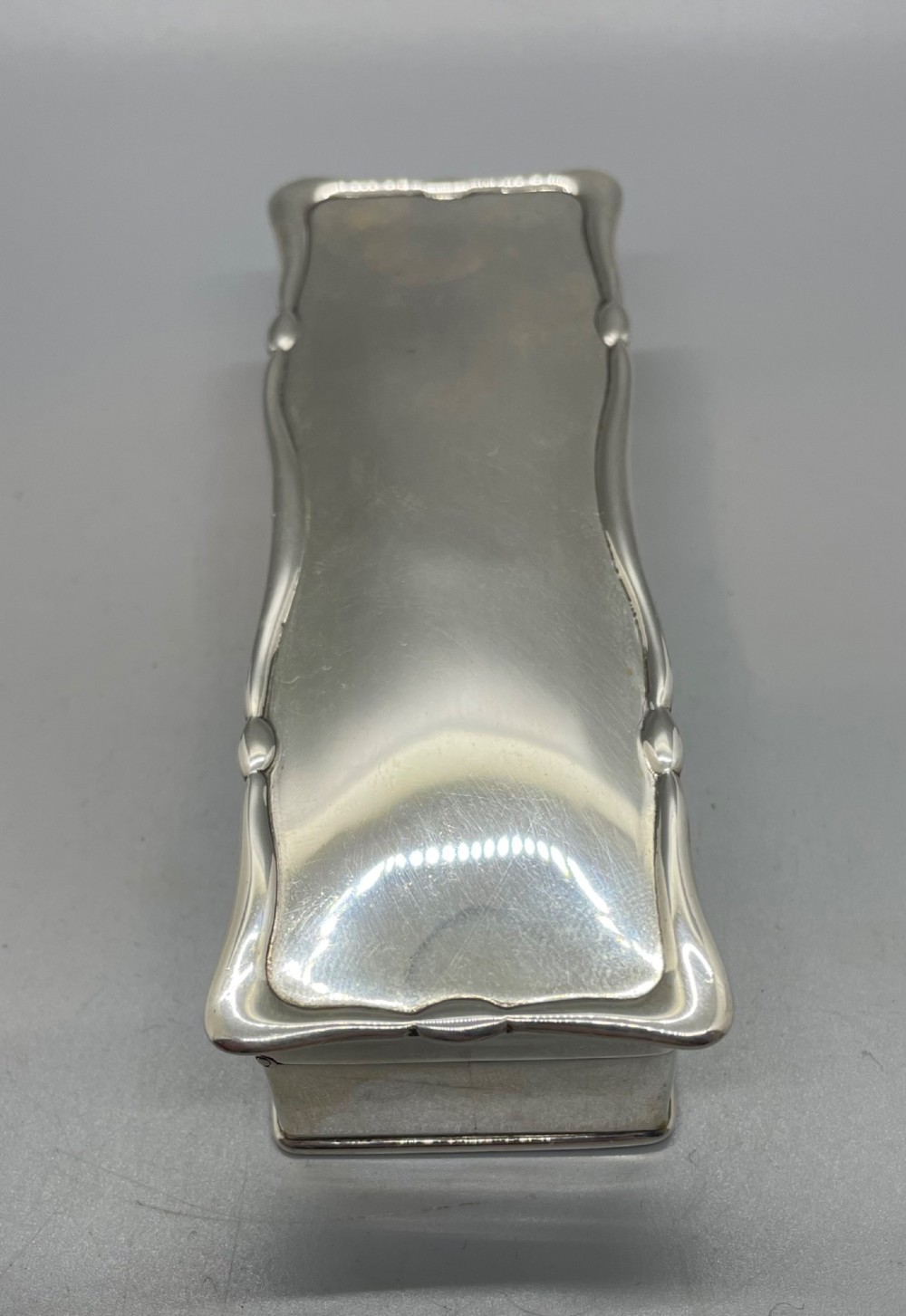 A rectangular Edwardian sterling silver box with a shaped, contoured lid rim and visible British hallmarks stamped on the front side. View V