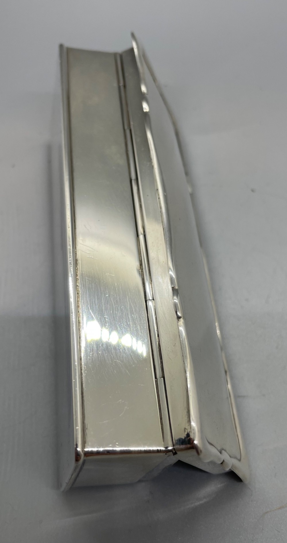 A rectangular Edwardian sterling silver box with a shaped, contoured lid rim and visible British hallmarks stamped on the front side. View VI
