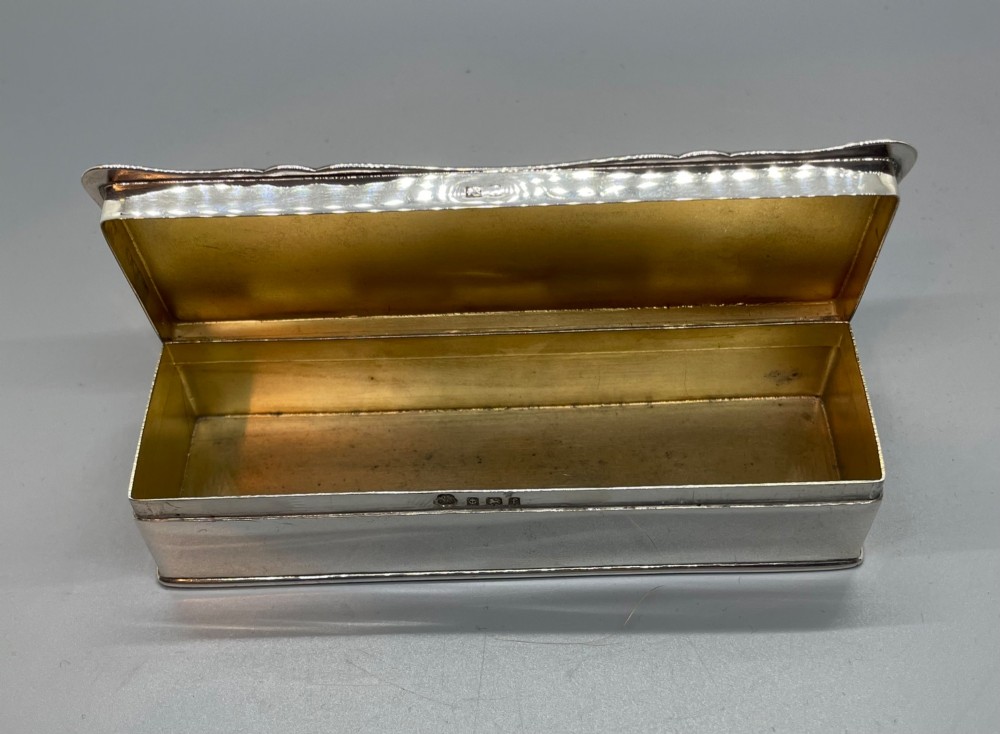 A rectangular Edwardian sterling silver box with a shaped, contoured lid rim and visible British hallmarks stamped on the front side. View VII
