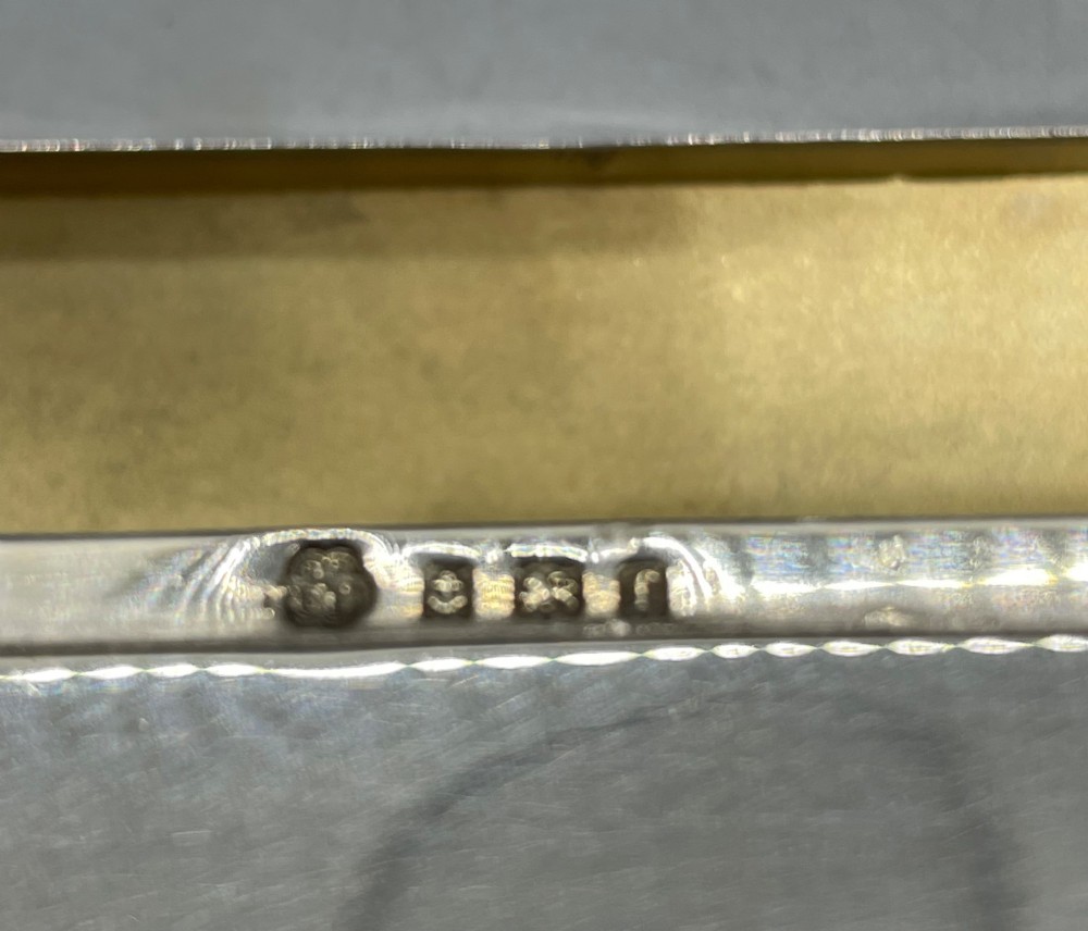 A rectangular Edwardian sterling silver box with a shaped, contoured lid rim and visible British hallmarks stamped on the front side. View VIII