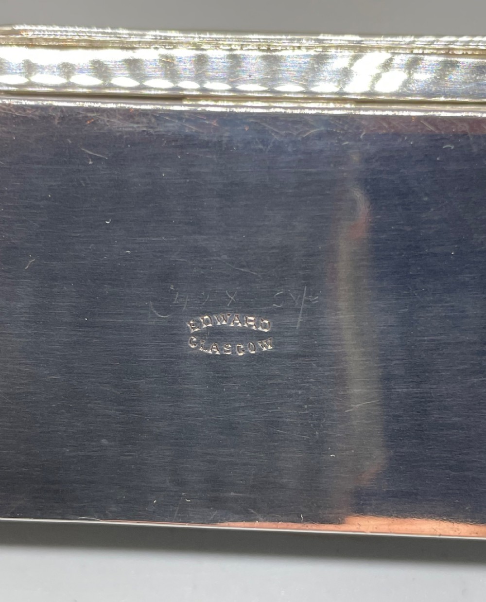 A rectangular Edwardian sterling silver box with a shaped, contoured lid rim and visible British hallmarks stamped on the front side. View IX
