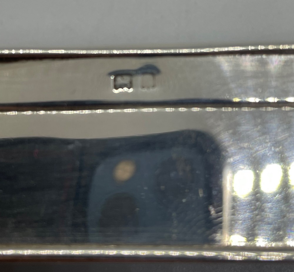 A rectangular Edwardian sterling silver box with a shaped, contoured lid rim and visible British hallmarks stamped on the front side. View X