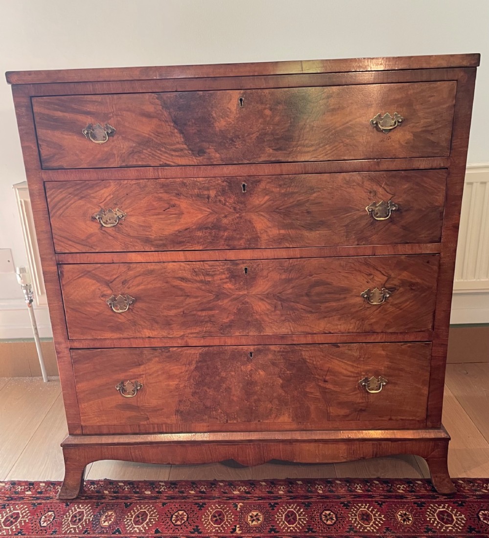 A George V walnut chest of drawers featuring four drawers with figured veneer fronts, brass drop handles, and bracket feet. View II