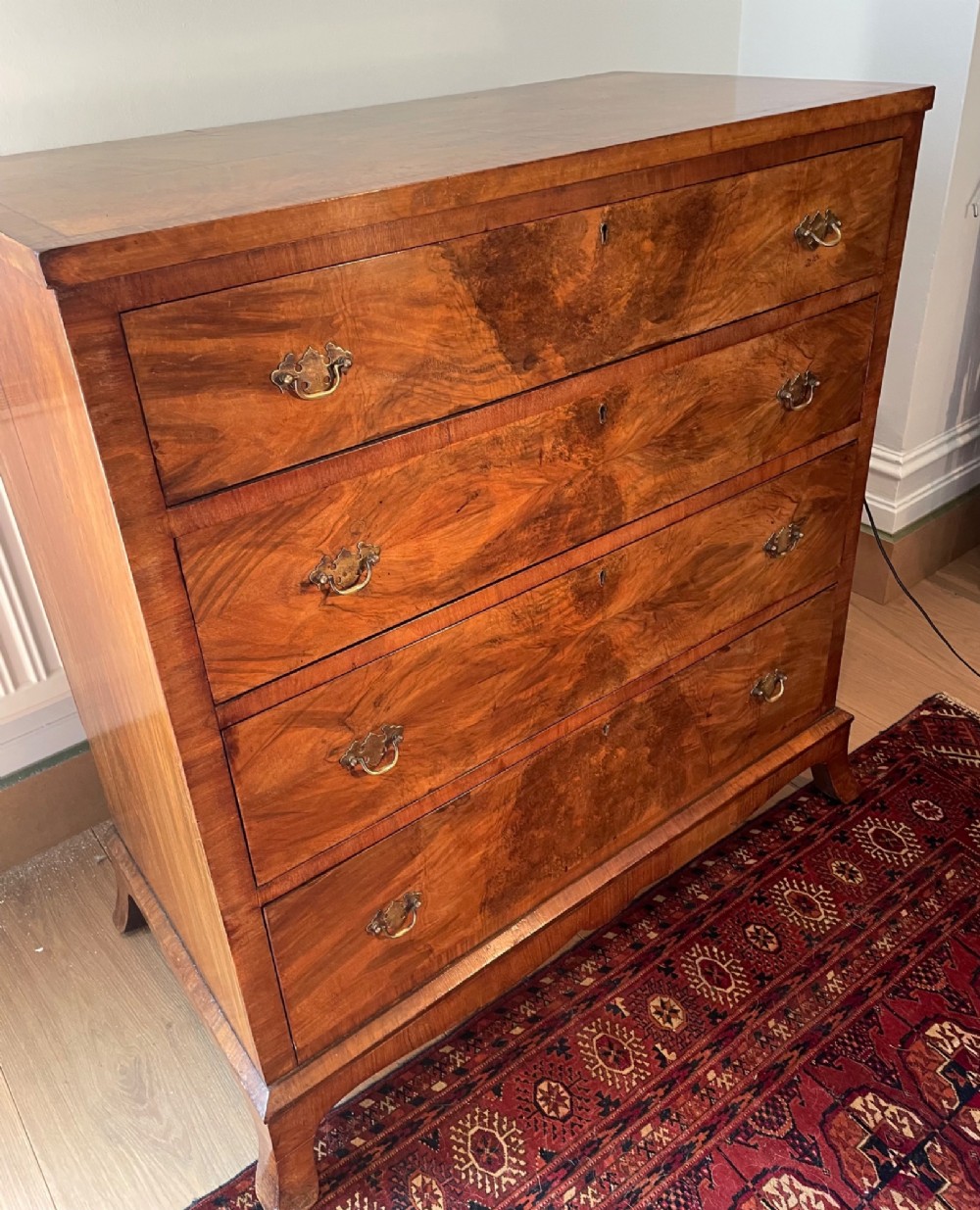 A George V walnut chest of drawers featuring four drawers with figured veneer fronts, brass drop handles, and bracket feet. View V