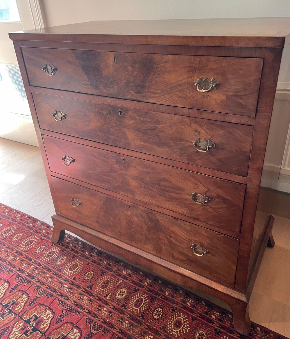 A George V walnut chest of drawers featuring four drawers with figured veneer fronts, brass drop handles, and bracket feet. View VI