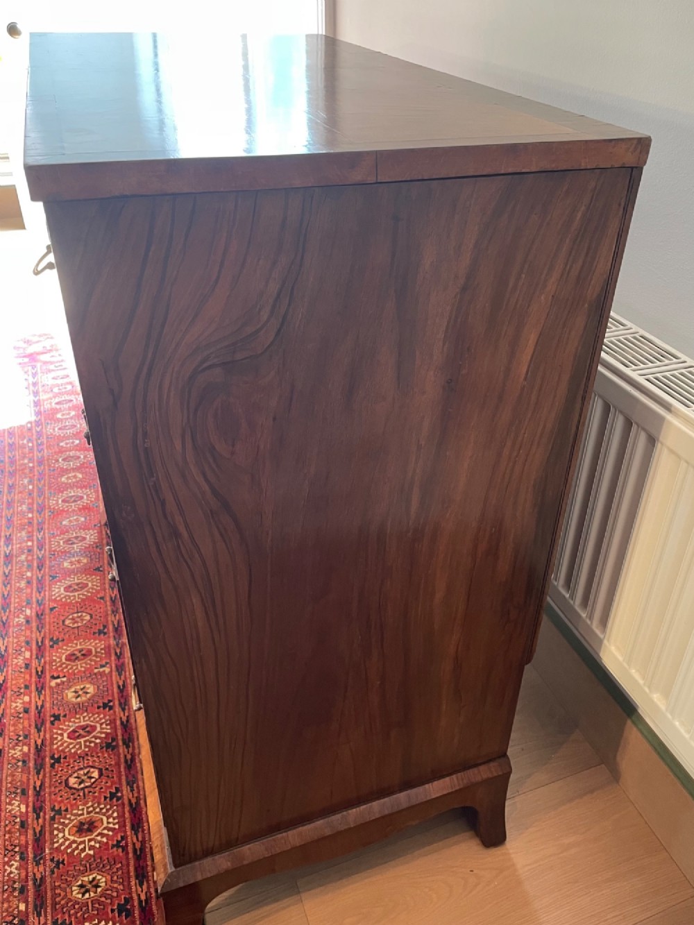 A George V walnut chest of drawers featuring four drawers with figured veneer fronts, brass drop handles, and bracket feet. View VIII