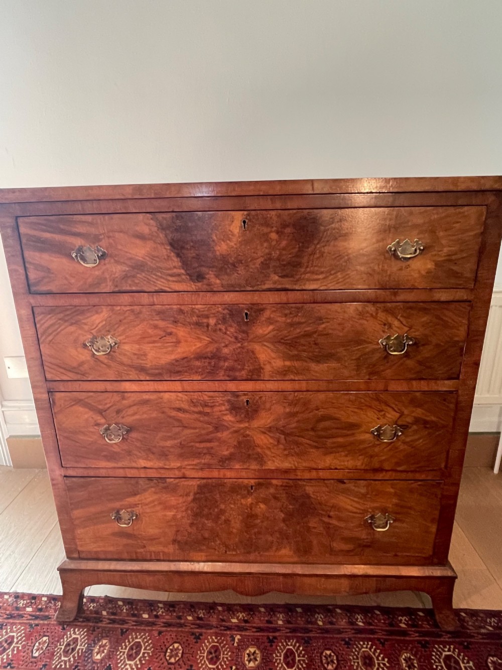 A George V walnut chest of drawers featuring four drawers with figured veneer fronts, brass drop handles, and bracket feet. View IX