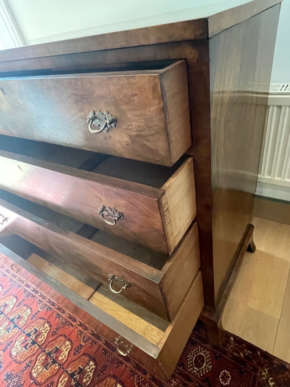 A George V walnut chest of drawers featuring four drawers with figured veneer fronts, brass drop handles, and bracket feet. View XII