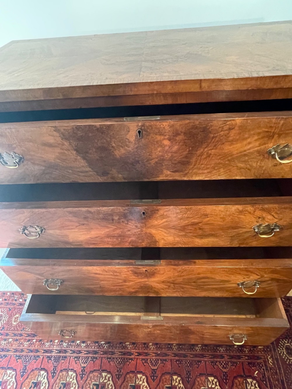 A George V walnut chest of drawers featuring four drawers with figured veneer fronts, brass drop handles, and bracket feet. View XIII