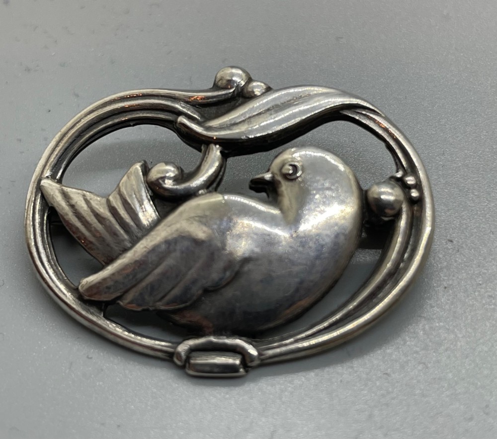 An oval sterling silver brooch depicting a bird in relief surrounded by stylised leaves and silver beads. View II