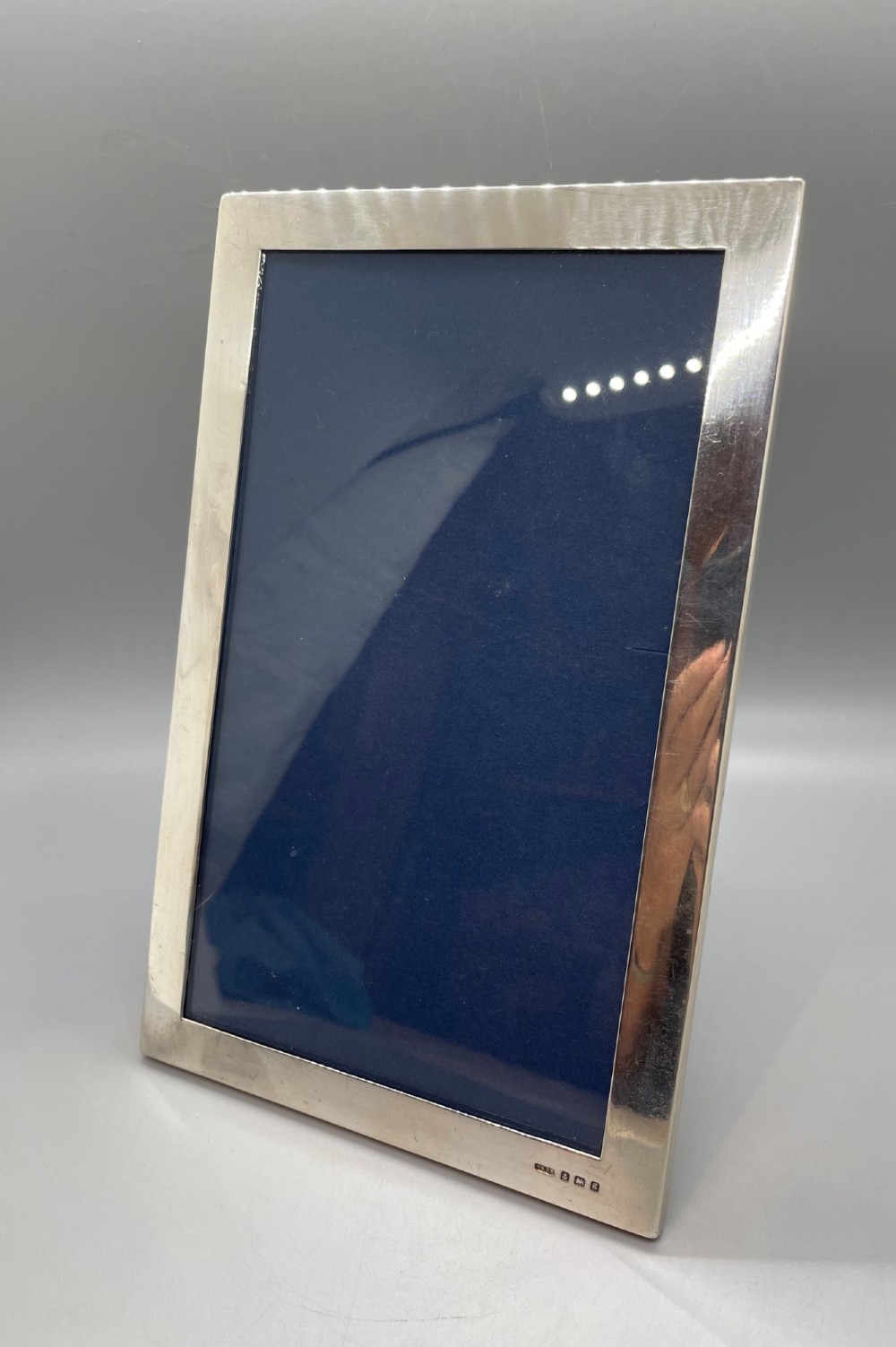 An Edwardian sterling silver rectangular photo frame featuring a plain polished border with visible English silver hallmarks at the base. View II