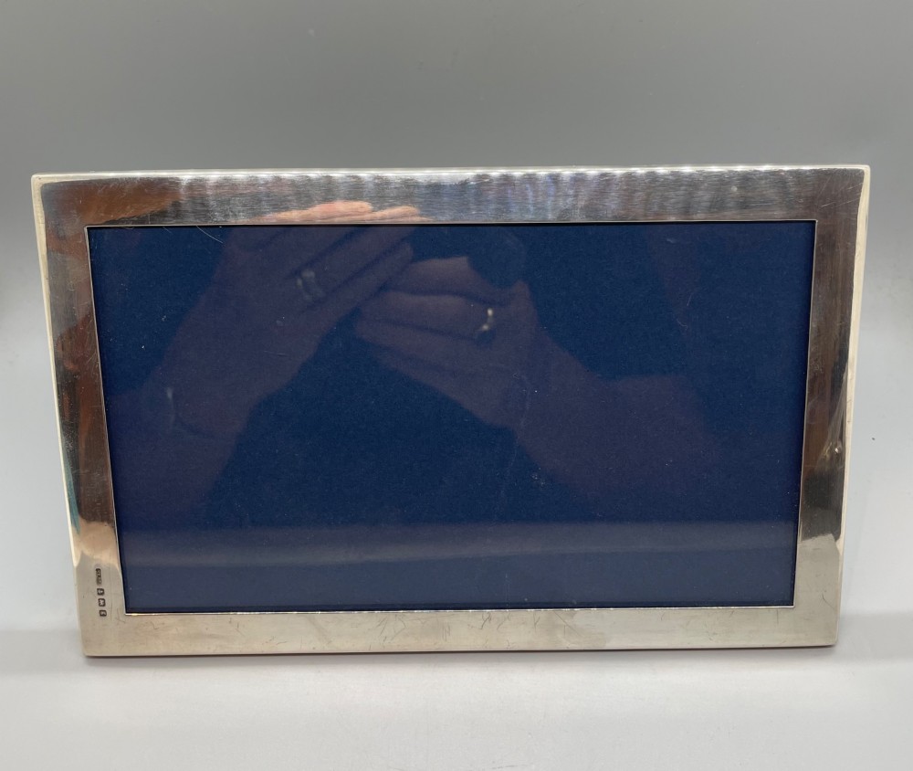 An Edwardian sterling silver rectangular photo frame featuring a plain polished border with visible English silver hallmarks at the base. View V