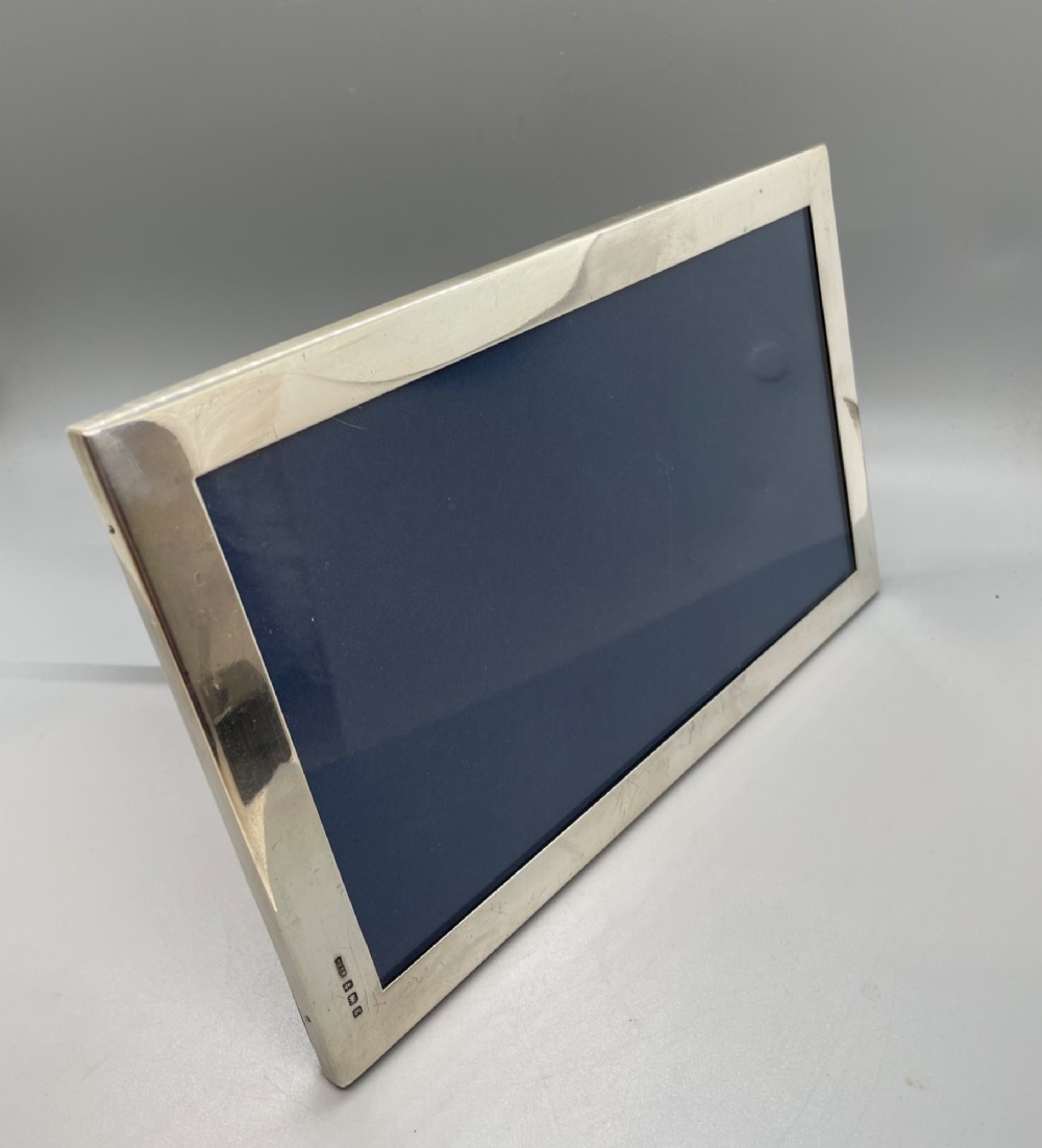 An Edwardian sterling silver rectangular photo frame featuring a plain polished border with visible English silver hallmarks at the base. View VI