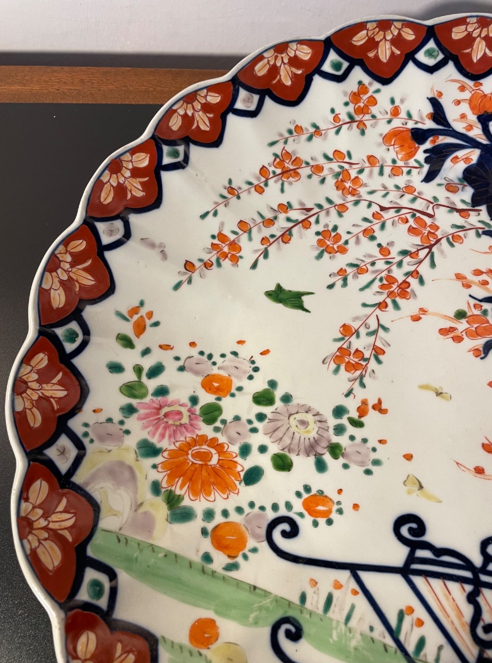 A circular Japanese Imari porcelain charger with a scalloped rim, featuring a hand-painted floral cart motif surrounded by cobalt blue and rust red enamel borders. View V