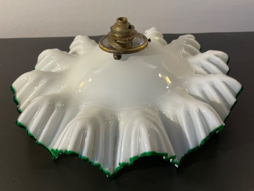 A white opaline glass lampshade with a fluted frilled edge trimmed in green glass, mounted with a brass top fixture.
