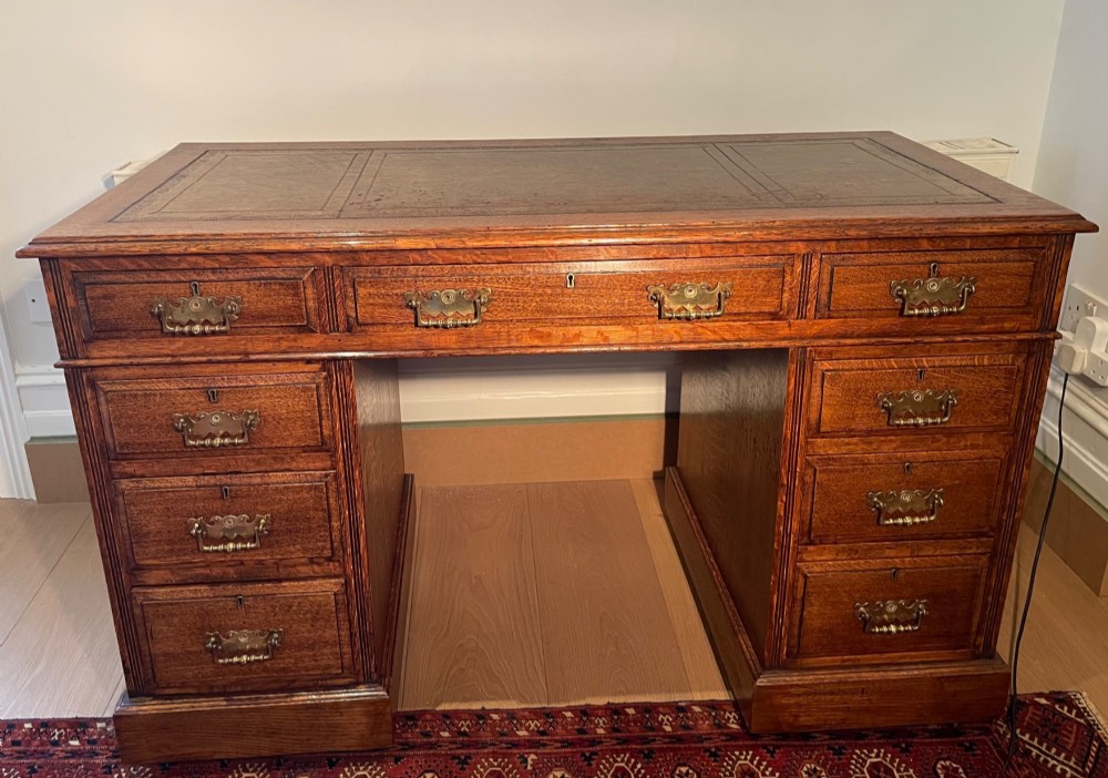 A Victorian oak pedestal desk featuring a gold-tooled leather writing top, nine drawers, and brass handles on a plinth base. View II