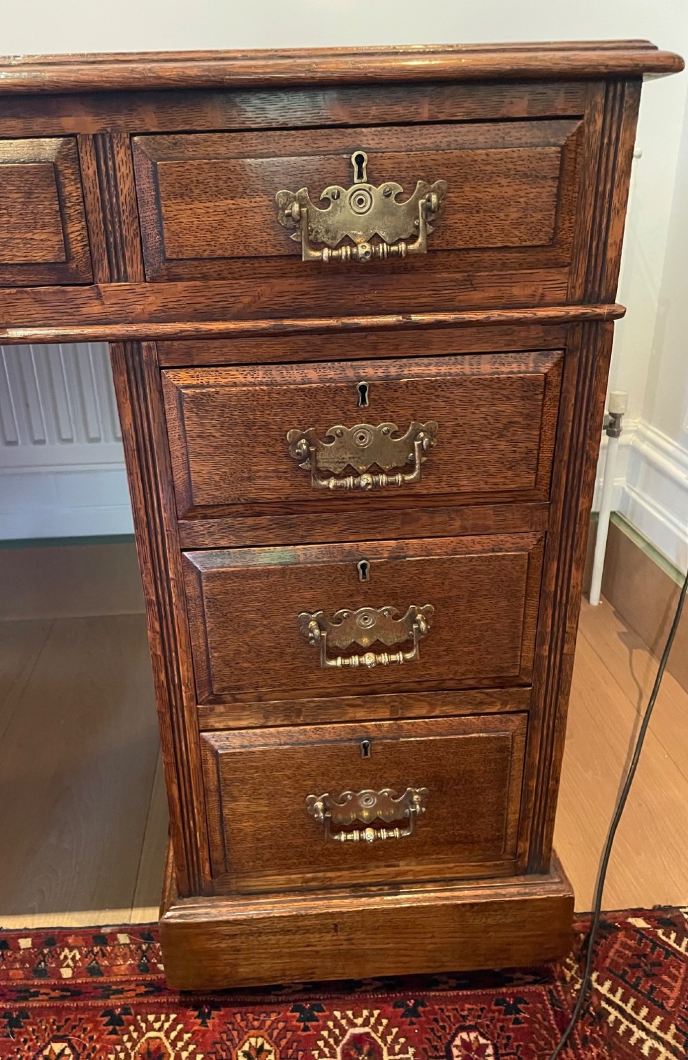 A Victorian oak pedestal desk featuring a gold-tooled leather writing top, nine drawers, and brass handles on a plinth base. View V
