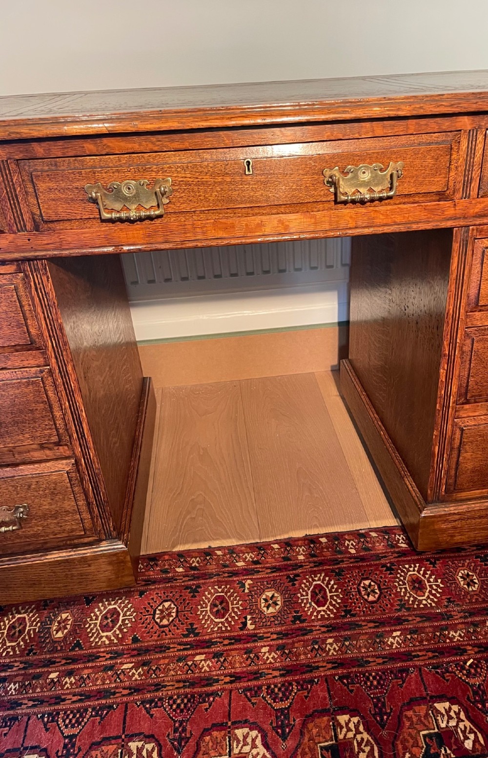 A Victorian oak pedestal desk featuring a gold-tooled leather writing top, nine drawers, and brass handles on a plinth base. View VI
