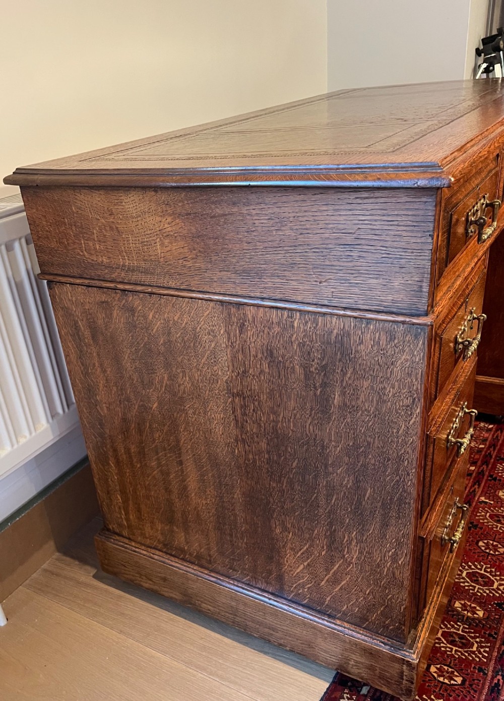 A Victorian oak pedestal desk featuring a gold-tooled leather writing top, nine drawers, and brass handles on a plinth base. View VII