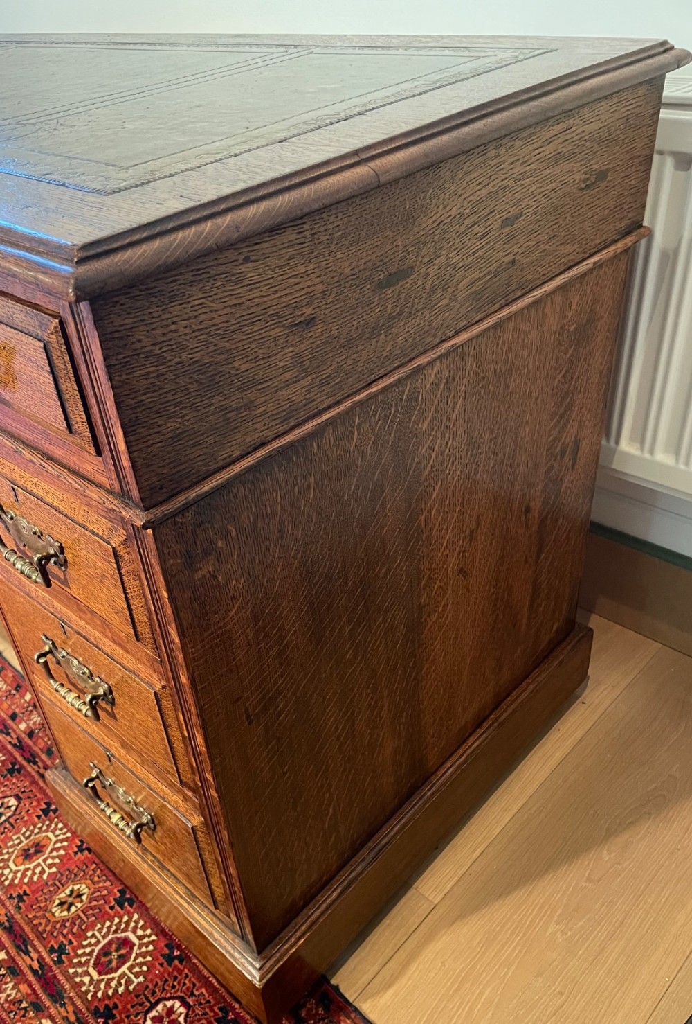 A Victorian oak pedestal desk featuring a gold-tooled leather writing top, nine drawers, and brass handles on a plinth base. View VIII