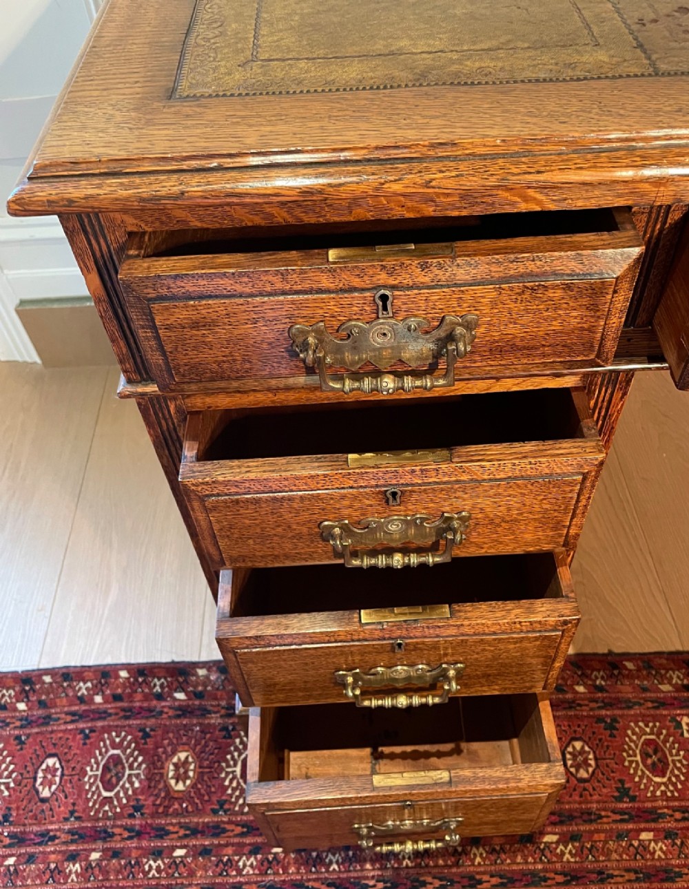 A Victorian oak pedestal desk featuring a gold-tooled leather writing top, nine drawers, and brass handles on a plinth base. View XI