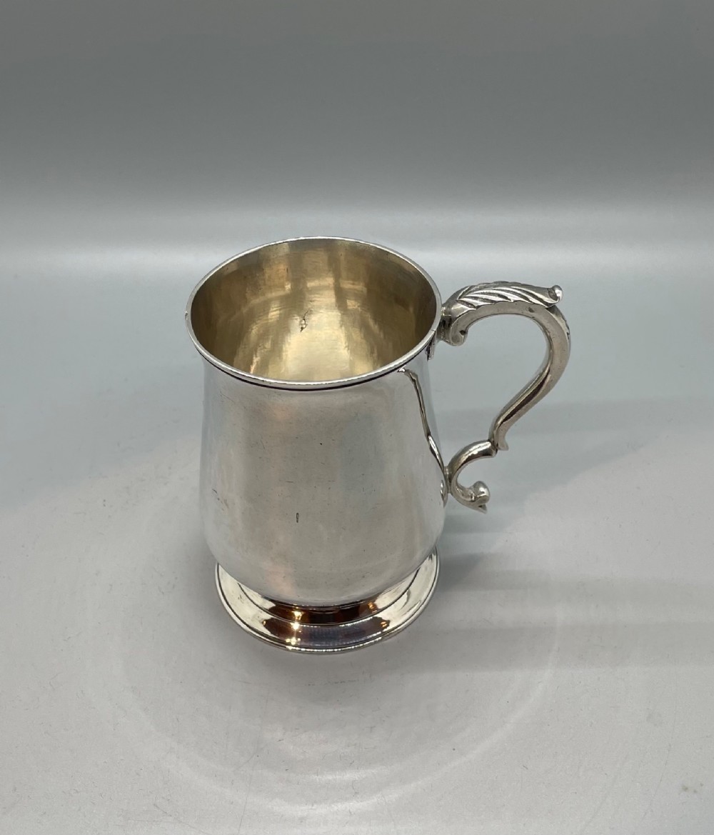 A Georgian sterling silver baluster-shaped mug featuring a leaf-capped double-scroll handle and a stepped circular base.