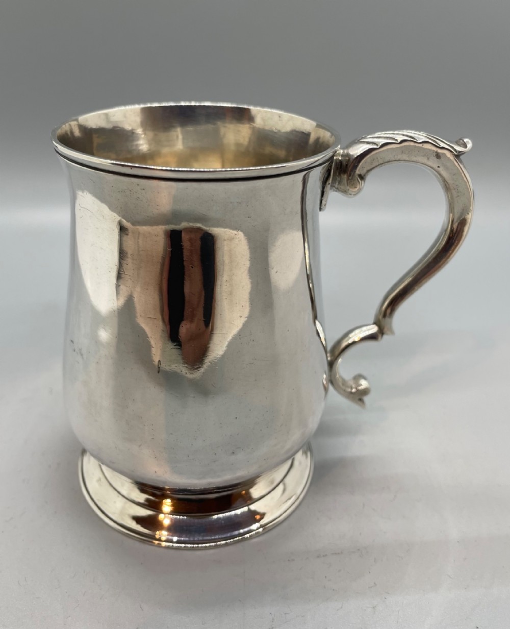 A Georgian sterling silver baluster-shaped mug featuring a leaf-capped double-scroll handle and a stepped circular base. View V