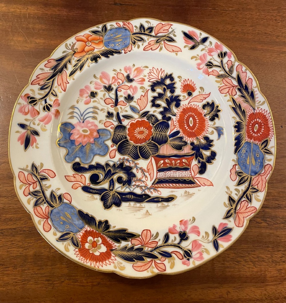 A set of three circular early nineteenth-century ceramic plates featuring hand-painted floral urn motifs in cobalt blue, iron red, and gold with scalloped edges. View VI