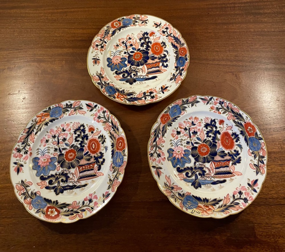 A set of three circular early nineteenth-century ceramic plates featuring hand-painted floral urn motifs in cobalt blue, iron red, and gold with scalloped edges. View VII