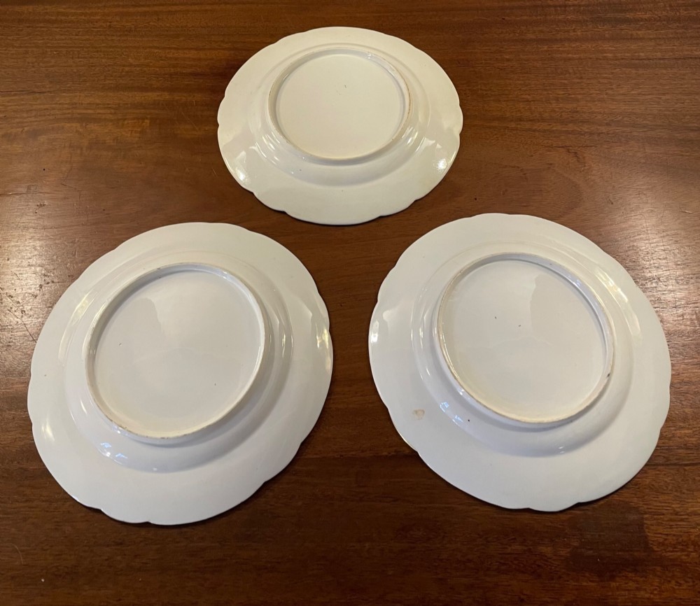 A set of three circular early nineteenth-century ceramic plates featuring hand-painted floral urn motifs in cobalt blue, iron red, and gold with scalloped edges. View VIII
