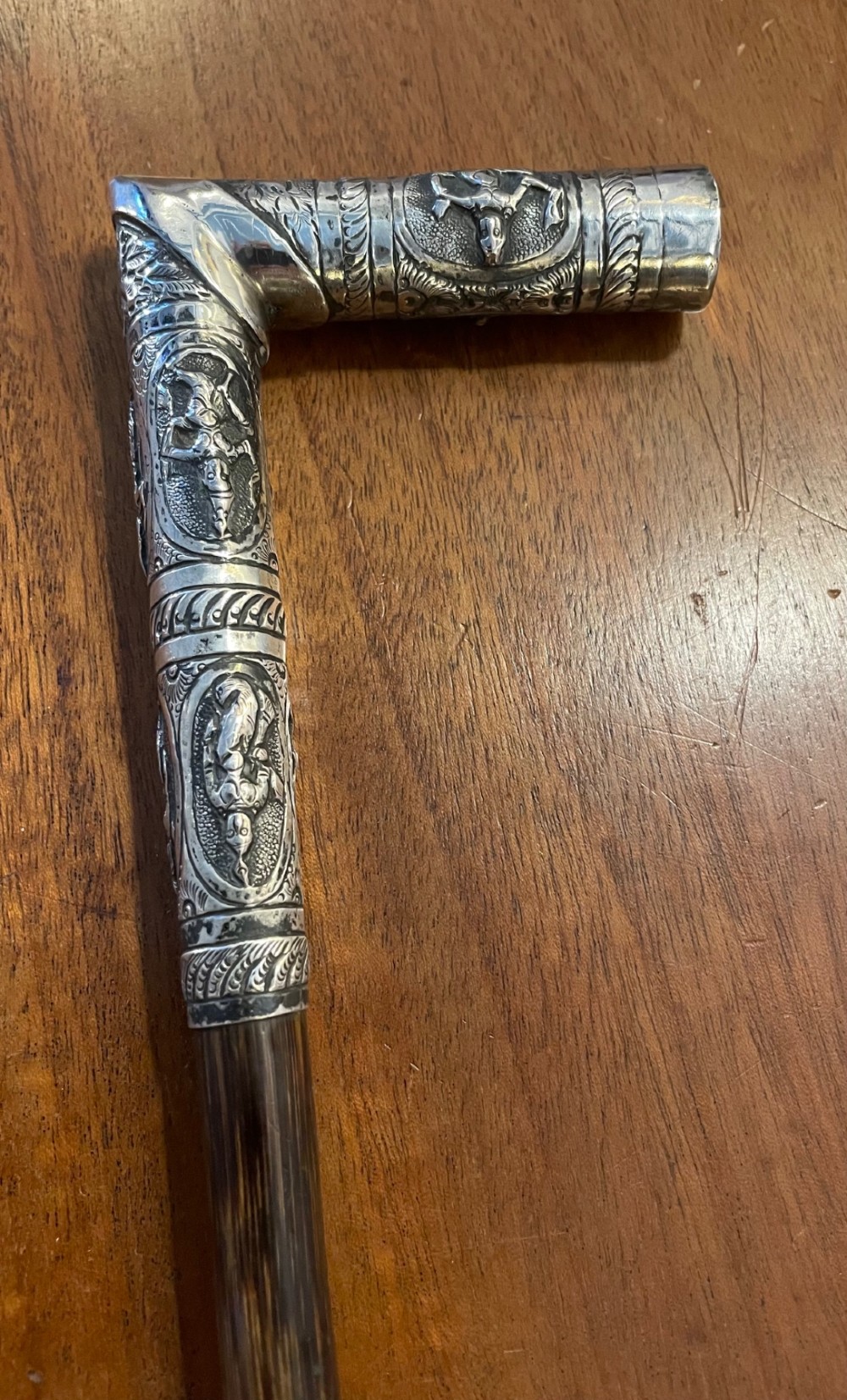 An antique walking stick with an embossed L-shaped silver handle featuring figurative motifs mounted on a dark brown bamboo shaft. View VIII