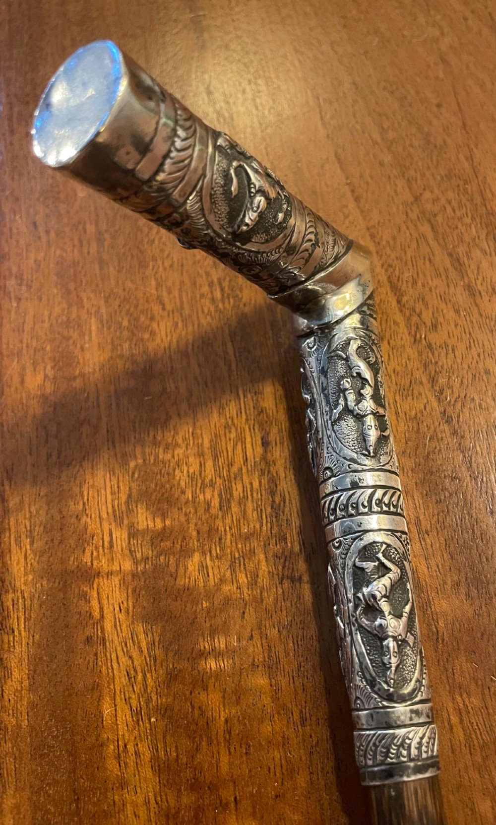 An antique walking stick with an embossed L-shaped silver handle featuring figurative motifs mounted on a dark brown bamboo shaft. View IX
