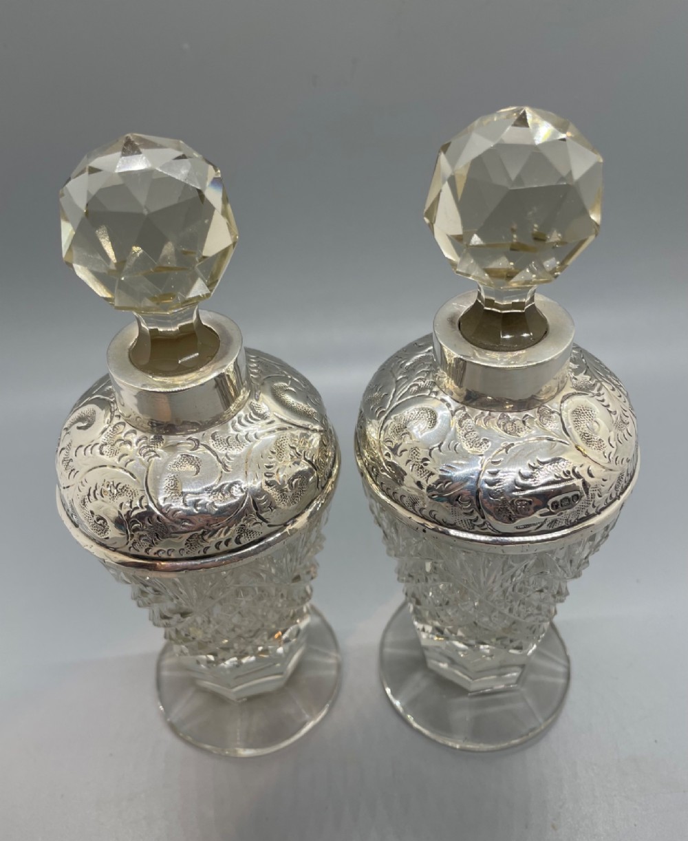 A pair of George V cut glass scent bottles featuring embossed sterling silver mounts and faceted glass stoppers. View II