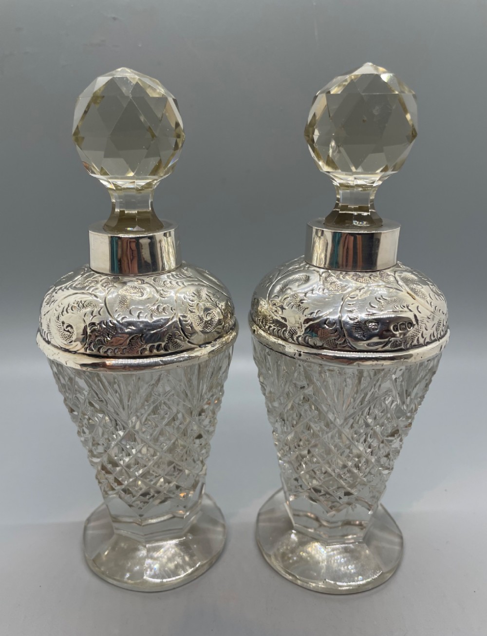 A pair of George V cut glass scent bottles featuring embossed sterling silver mounts and faceted glass stoppers. View III