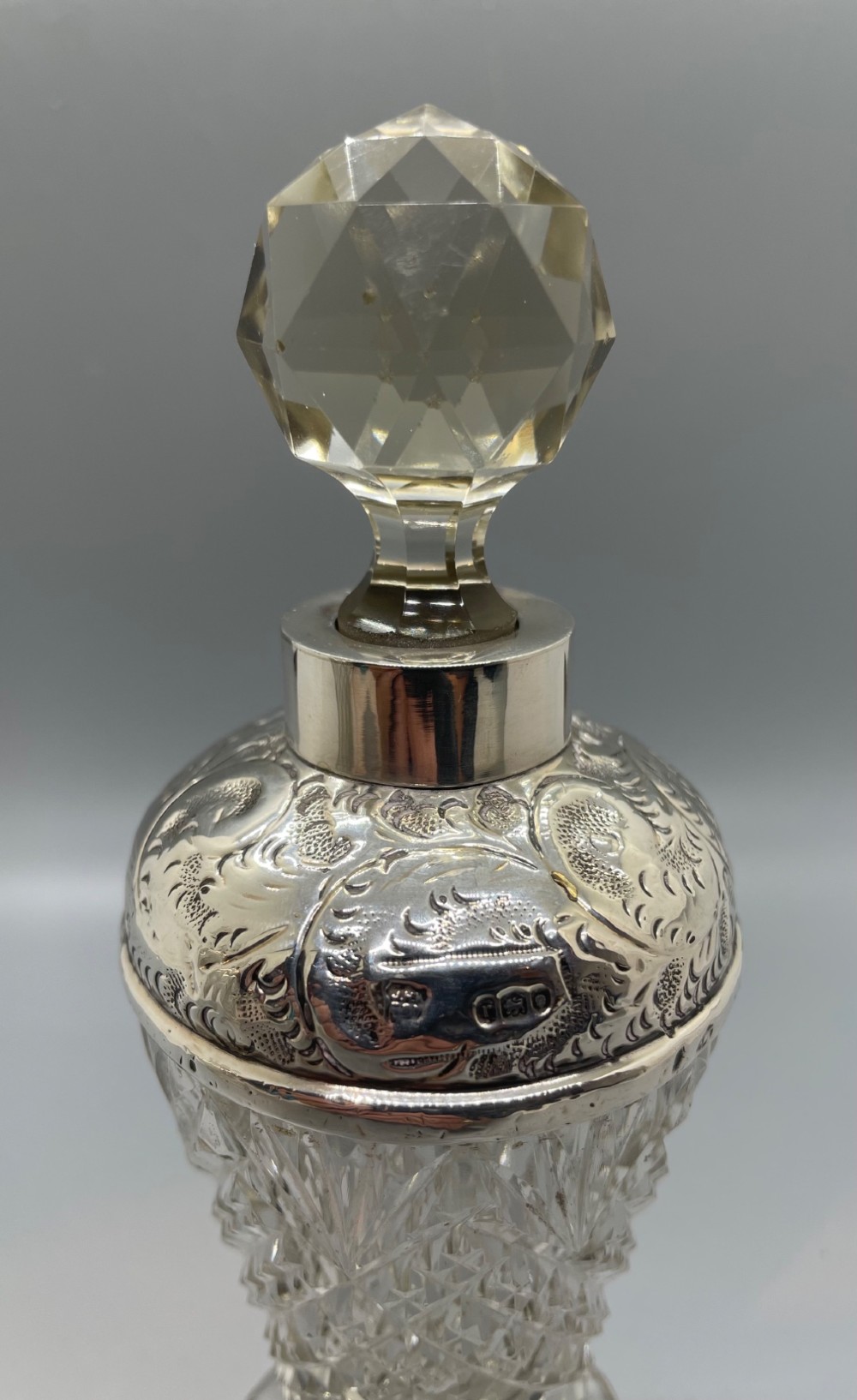 A pair of George V cut glass scent bottles featuring embossed sterling silver mounts and faceted glass stoppers. View IV