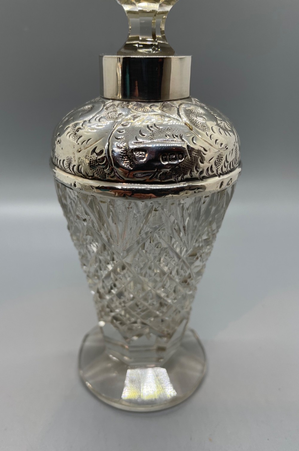 A pair of George V cut glass scent bottles featuring embossed sterling silver mounts and faceted glass stoppers. View V