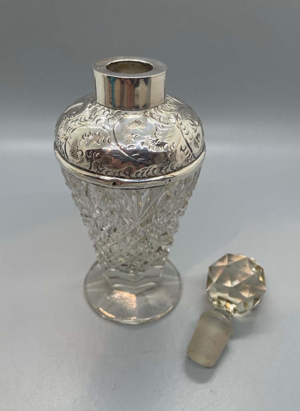 A pair of George V cut glass scent bottles featuring embossed sterling silver mounts and faceted glass stoppers. View VI