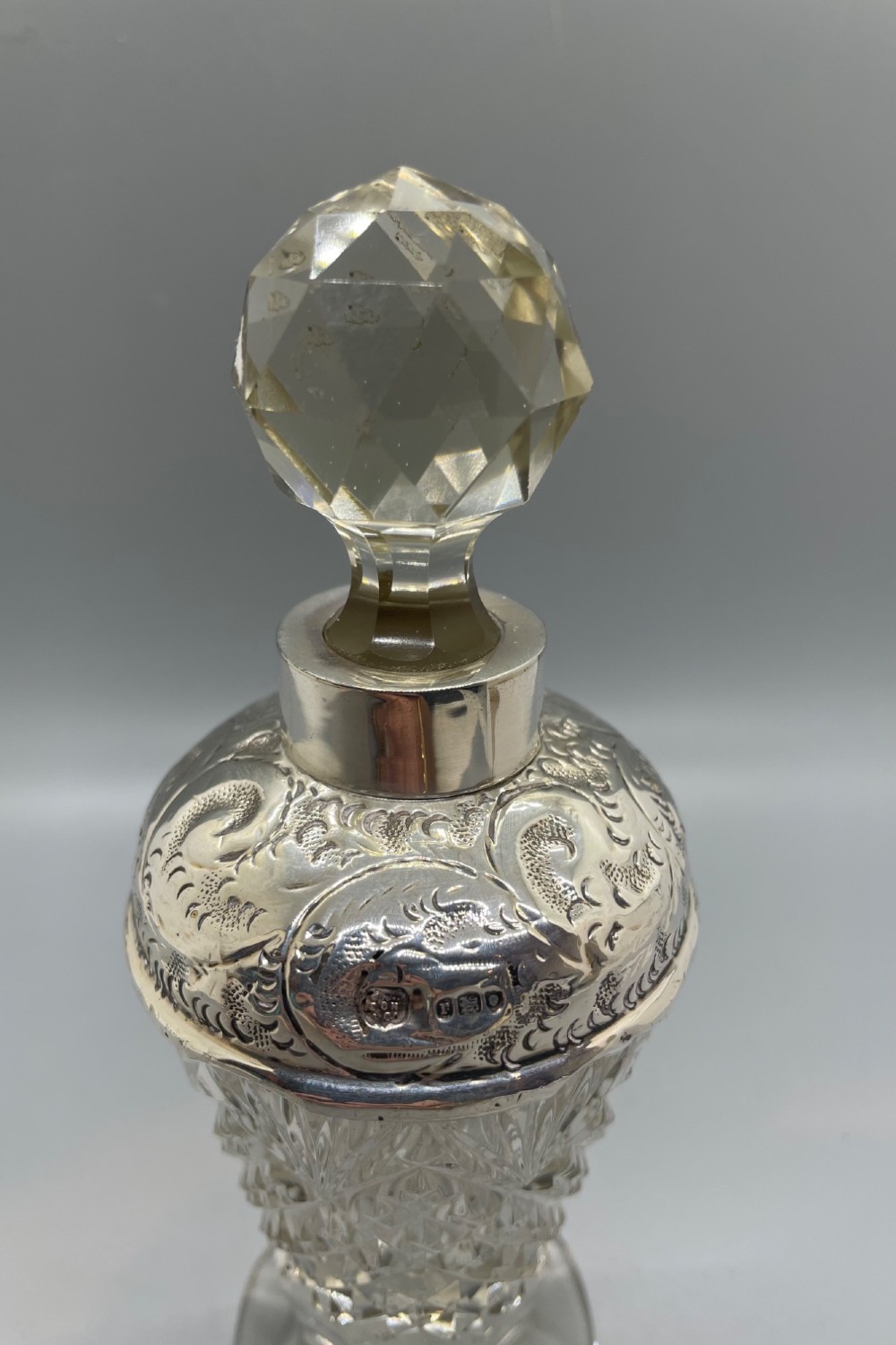 A pair of George V cut glass scent bottles featuring embossed sterling silver mounts and faceted glass stoppers. View VIII