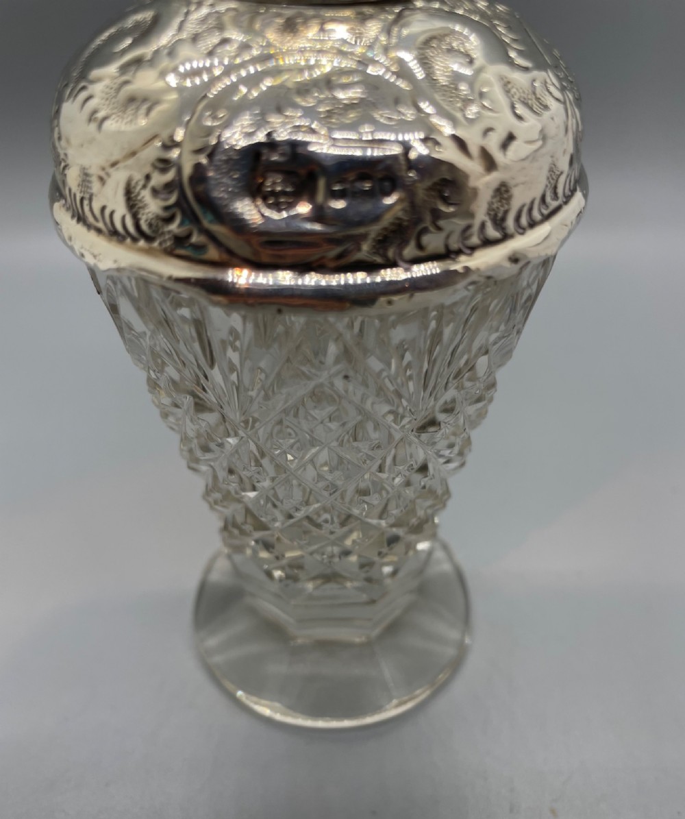 A pair of George V cut glass scent bottles featuring embossed sterling silver mounts and faceted glass stoppers. View IX