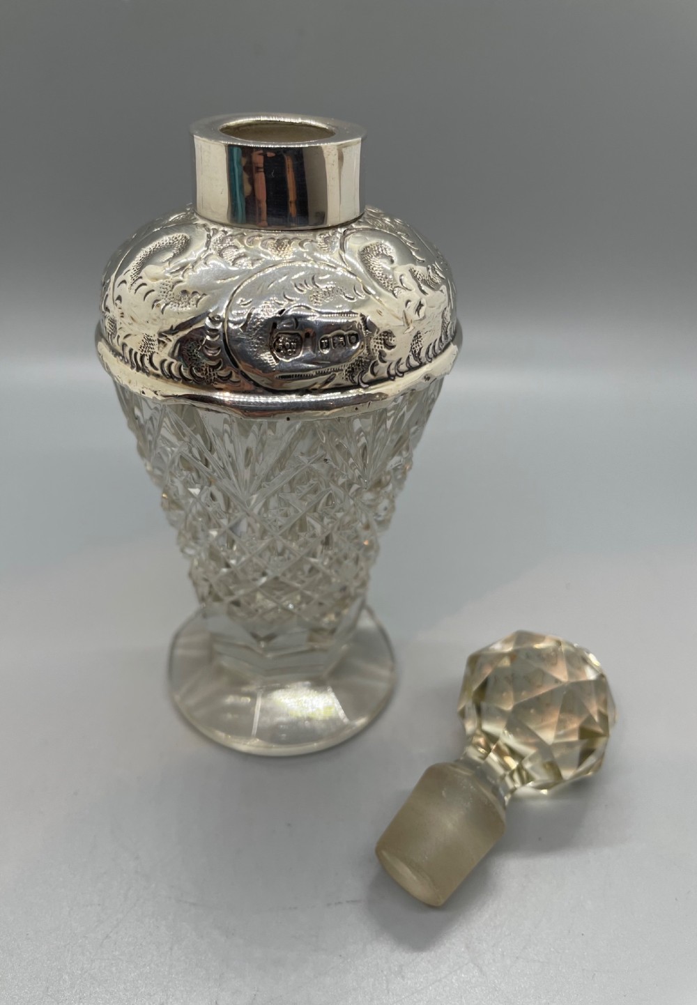 A pair of George V cut glass scent bottles featuring embossed sterling silver mounts and faceted glass stoppers. View X