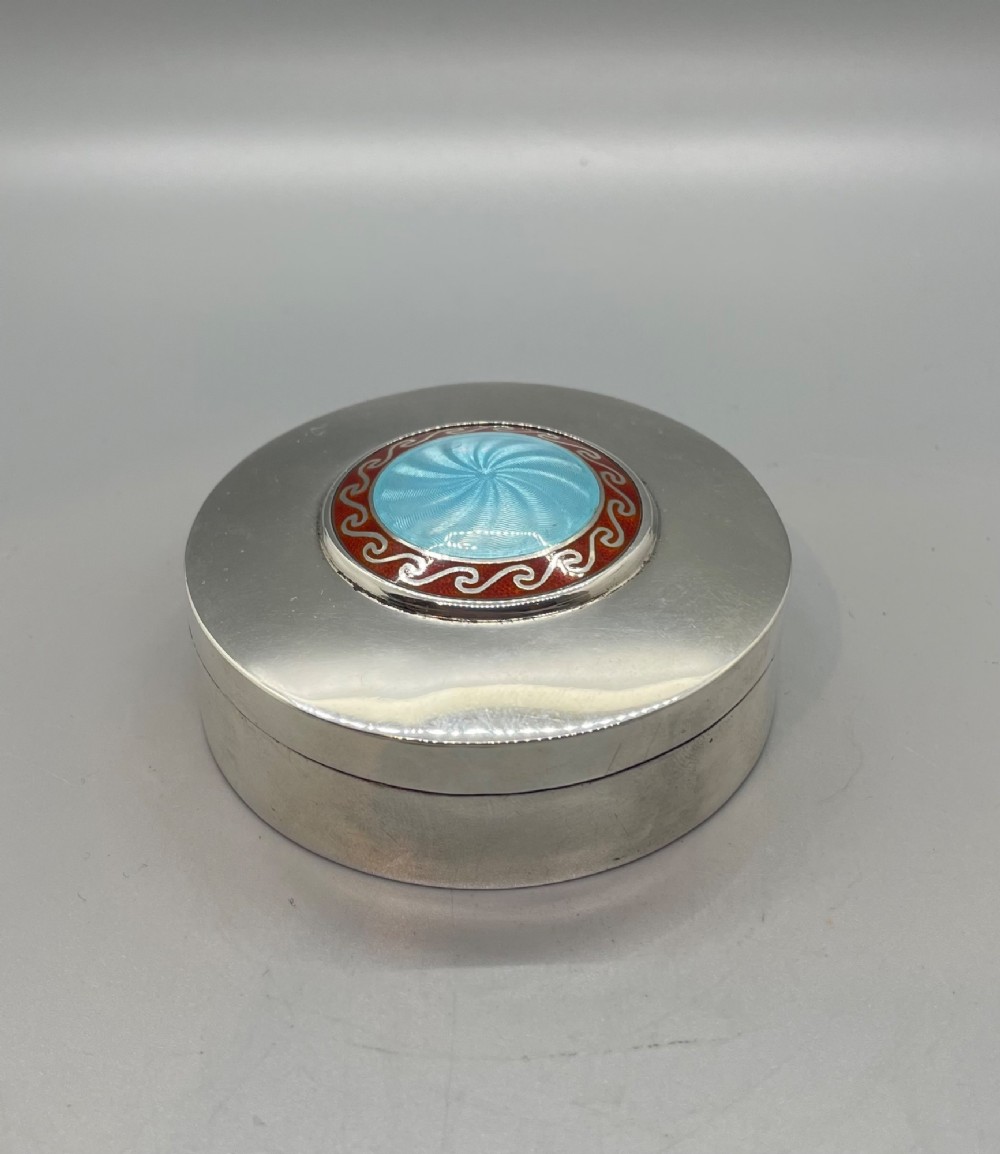 A circular sterling silver trinket box featuring a central light blue guilloche enamel medallion encircled by a red enamel border.